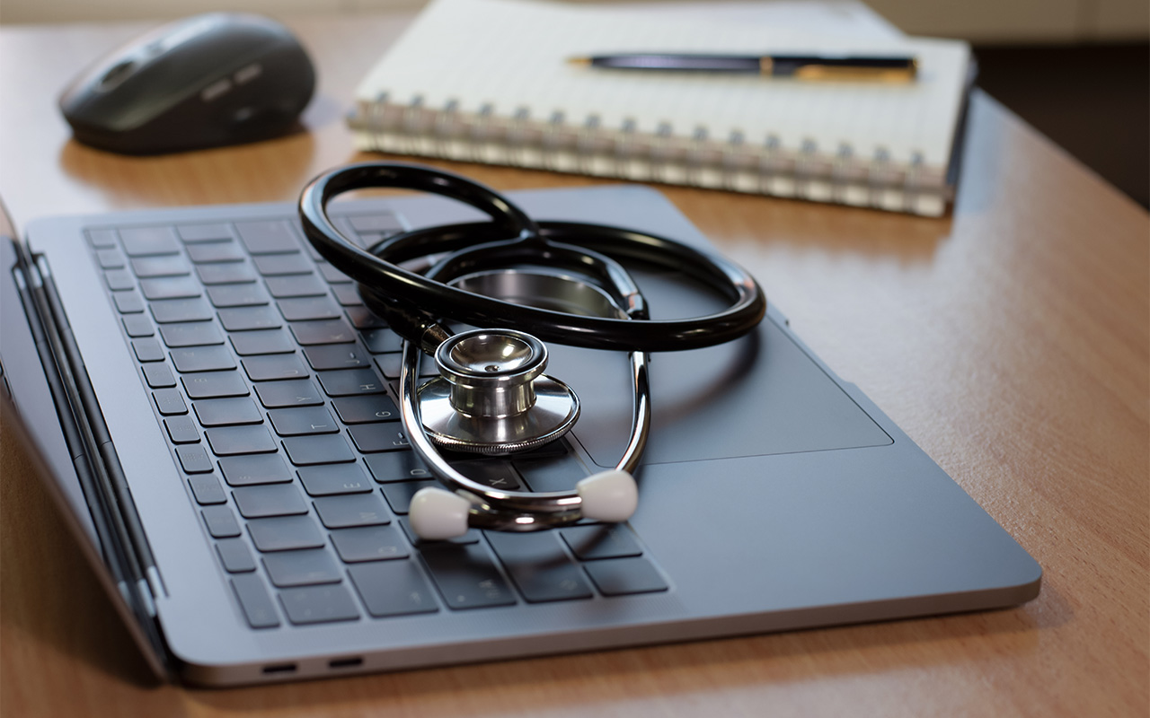 Image of medical stethoscope on laptop computer, notebook, pen and wireless mouse isolated on wooden desk.