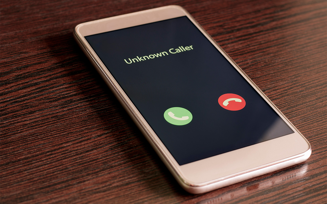 Photo of white smartphone with incoming call from an unknown number on a wood table background.