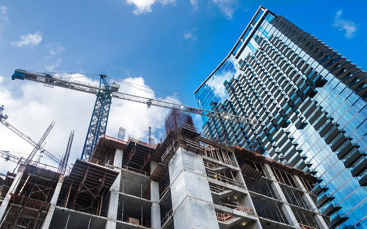 High rise building under construction with large cranes and a blue sky background.
