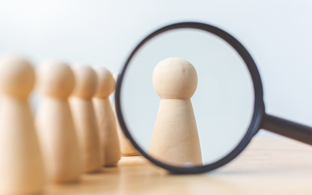 image of game pieces with one piece in a magnifying glass, depicting successful team leader concept