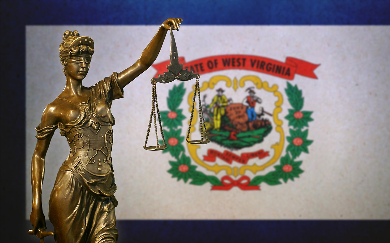 Close-up of a small bronze statuette of Lady Justice before a flag of West Virginia.