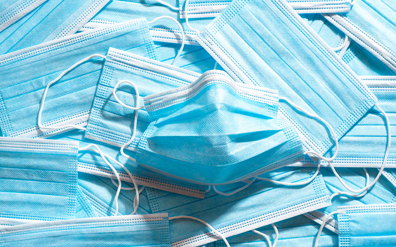 Background of blue medical masks in bright light, top view.