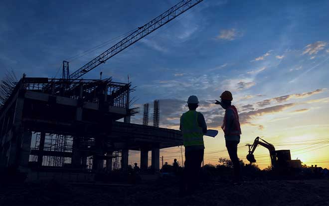 Photo of a construction site and two workers against a sunset