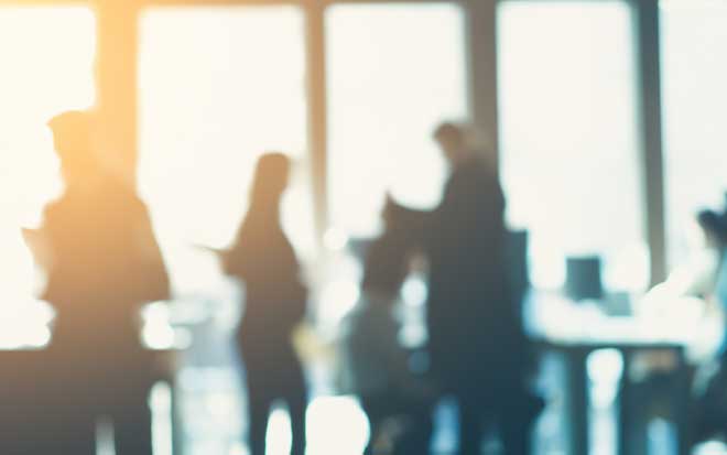 Blurry silhouette of people sitting at desks and standing in an office space