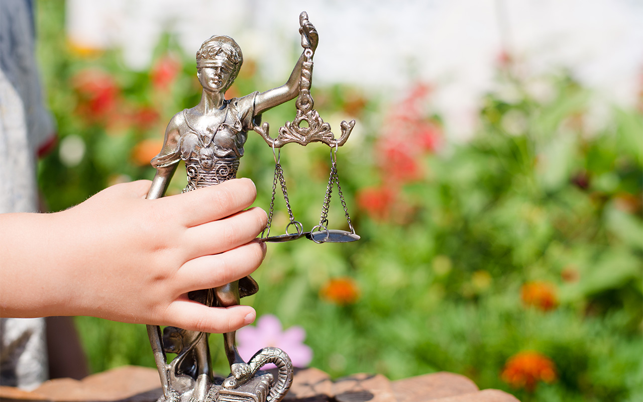 Kid's hand holding sculpture of themis, femida or justice goddess on green leaves natural bokeh background